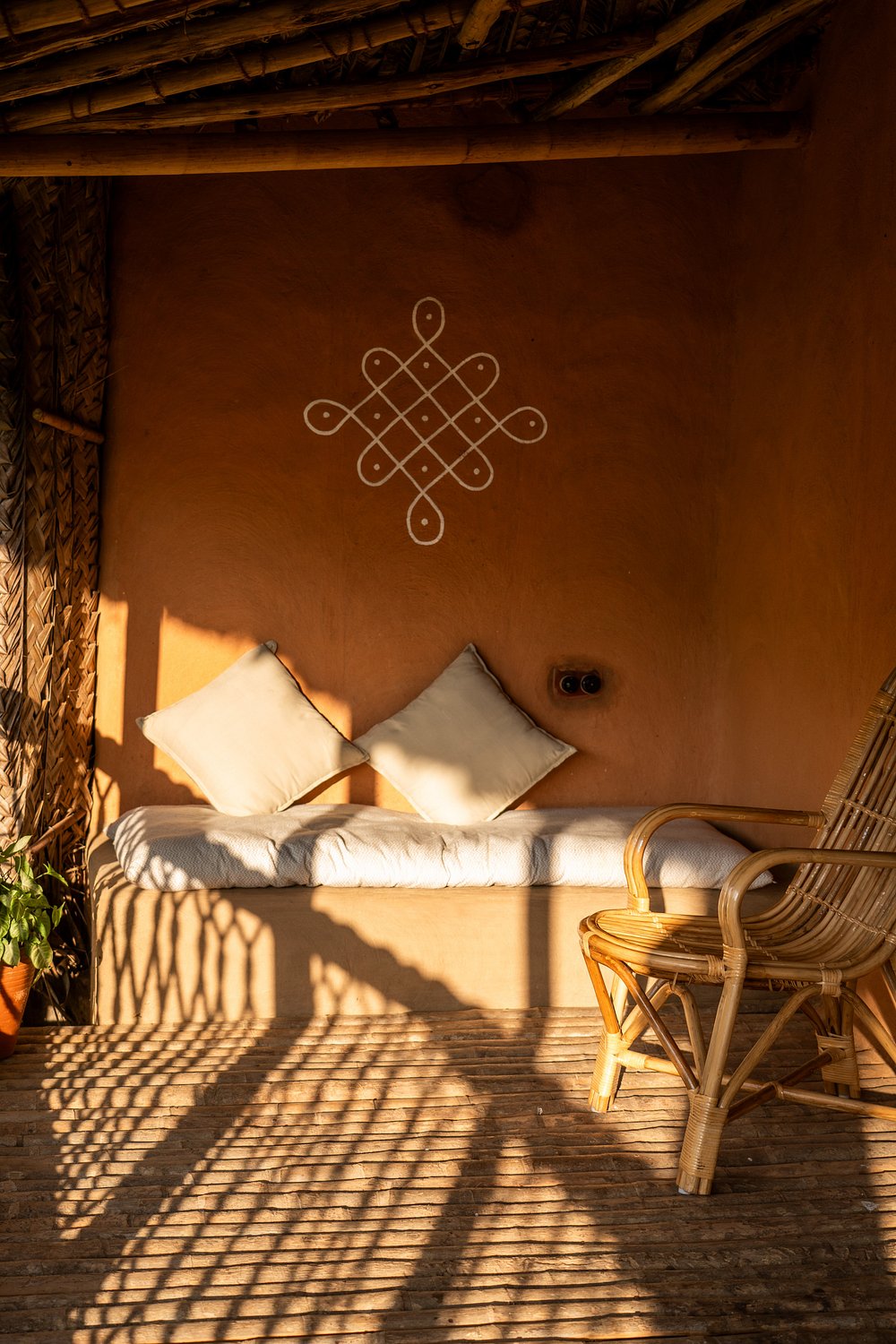Kolam art on terracotta wall with cushioned bench